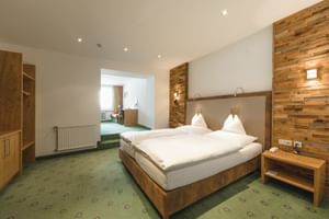 Chambre d'hôtel double moderne avec lit en bois, mur d'accent en bois, moquette verte à motifs et coin salon avec vue montagne.