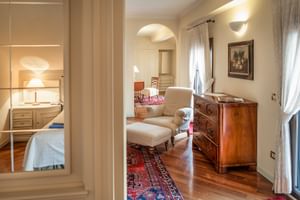 Elegante Loft-Suite mit cremefarbenem Sessel, Holzkommode, Perserteppich auf Parkettboden und Blick ins Schlafzimmer mit weißer Bettwäsche.