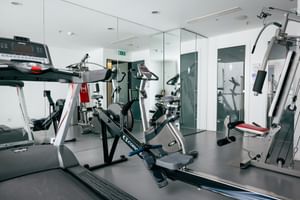 Moderner Fitnessraum im Macarico Beach Hotel mit Laufband, Heimtrainer, Kraftgeräten und Spiegelwänden in hellem weißen Interieur.