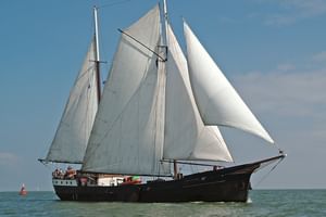 Traditionelles zweimastiges Segelschiff Wapen fan Fryslan mit weißen Segeln auf ruhigem blauen Wasser unter teilweise bewölktem Himmel.
