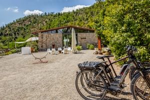 Steingebäude mit Terrasse und weißen Sonnenliegen im Agriturismo Le Valli in Casciana Terme. Fahrräder auf Kiesplatz, Hügel im Hintergrund.