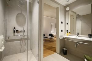 Modernes Badezimmer im Giardino Verdi Riva mit Glasduschkabine, weißem Waschtisch mit Spiegel und Blick ins angrenzende Schlafzimmer mit Holzboden.