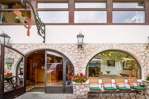 Hoteleingang mit gewölbter Tür in Steinfassade, Holzliegen mit roten Geranien und traditioneller Laterne im Hotel Post am See Traunkirchen.