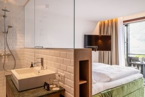 Modernes Hotelzimmer im Post Traunkirchen mit weißen U-Bahn-Fliesen, offenem Bad, grünem Samtbett und Balkon mit Seeblick.