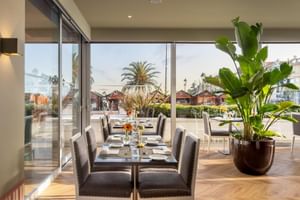 Modernes Restaurant-Interieur im Hotel Baia mit grauen Polsterstühlen, gedeckten Tischen und bodentiefen Fenstern mit Blick auf Cascais.