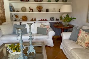 Salon lumineux au Can Quatre Sóller avec canapés blancs, coussins décoratifs, table basse en verre et étagères blanches avec céramiques.