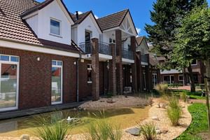 Modernes Hotel Upstalsboom Gebäude mit weißen Wänden, roten Ziegeldächern, Backsteinsäulen und Balkonen. Angelegter Garten mit Teich im Vordergrund.