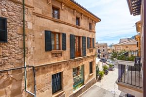 Bâtiment traditionnel en grès à Pollenca avec volets verts et toit de tuiles, donnant sur une rue calme à l'architecture méditerranéenne.