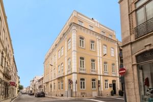 Gelbes Eckgebäude des Universal Boutique Hotels mit weißen Verzierungen und Balkonen an einer Kopfsteinpflasterstraße in Figueira da Foz.