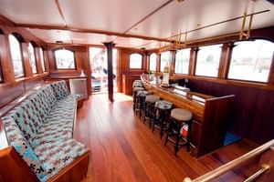 Innenraum der Mare fan Fryslan Schiffsbar mit Holzvertäfelung, gebogenen Sitzplätzen mit gemusterter Polsterung, Bartheke mit Hockern und Fenstern.