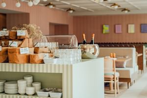 Moderne Frühstückstheke im Hotel zum Hirschen Salzburg mit Holzbrotboxen, Gläsern, Tellern, Sektflaschen und Essbereich im Hintergrund.