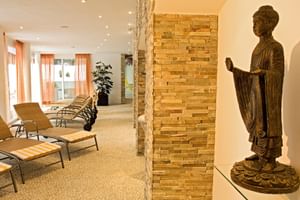 Moderner Wellnessbereich mit Entspannungsliegen, Steinziegelsäulen, Buddha-Statue und orangenen Vorhängen im Hotel Alpen Residence Ehrwald.