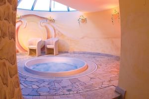 Runder Whirlpool im Wiesnerhof Sterzing mit Steinboden, Holzliegen und Oberlicht in warmtonigem Spa-Raum.