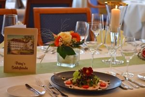 Feine Tischdeckung in der Schlossstube des Schloss Hotel Petry mit Gourmetgericht, Weingläsern, Kerze und Menükarte mit Schlossbild.
