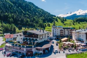 Luftaufnahme des Hotel Mein Almhof Komplexes in einem österreichischen Alpental mit schneebedeckten Bergen, grünen Wiesen und bewaldeten Hügeln.