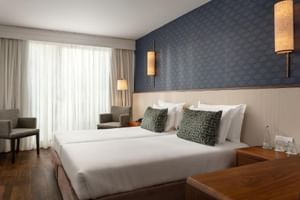 Modernes Doppelzimmer im Hotel Baia Cascais mit weißem Bett, blau gemusterter Wand, Holzschreibtisch, grauem Sessel und Hängeleuchten.