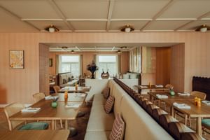 Moderner Frühstücksraum im Hotel zum Hirschen Salzburg mit Holztischen, Korbstühlen, beiger Sitzbank und Kassettendecke.