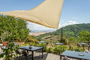 Außenterrasse mit Tischen und Stühlen unter beigem Sonnensegel im Le Valli Agriturismo in Casciana Terme mit Blick auf toskanische Hügel.