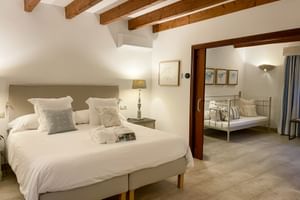Chambre spacieuse avec poutres apparentes, lit double beige et pièce adjacente avec lit en métal au Can Quatre Soller.