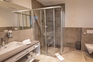 Modernes Badezimmer im Hotel Ertl in Spittal mit Glasduschkabine, Marmorwaschtisch, Wandtoilette und beigefarbenen Fliesen.