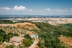 Luftaufnahme des Agriturismo Le Valli in Casciana Terme mit Steinhaus, Pool und toskanischen Hügeln mit Olivenhainen und Feldern.