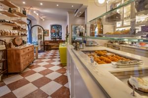 Hotel-Frühstücksbuffet mit Glasvitrinen voller Gebäck und Speisen, kariertem Boden und Holzregalen mit Produkten.