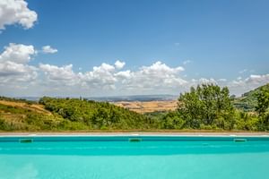 Türkisfarbener Pool im Le Valli Agriturismo in Casciana Terme mit Panoramablick auf toskanische Hügel unter blauem Himmel mit weißen Wolken.