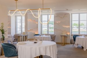 Elegantes Restaurantinterieur im Fleur de Loire Blois mit weißen Tischdecken, blauen Samtstühlen, künstlerischer Wellenbeleuchtung und Wanddekoration.