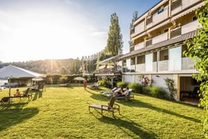 Mehrstöckiges Hotelgebäude mit Balkonen überblickt große grüne Rasenfläche mit Gartenmöbeln, Sonnenschirmen und entspannenden Gästen im goldenen Sonnenlicht.