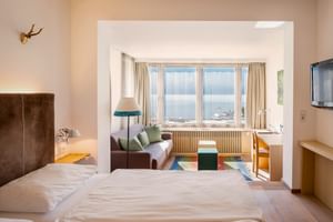 Geräumiges Doppelzimmer im Hotel Post am See Traunkirchen mit Seeblick, Sitzbereich, Holzmöbeln und buntem Teppich.