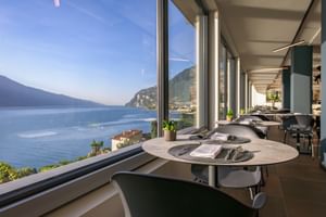 Modernes Restaurant-Interieur der Villa Dirce in Limone mit Panoramafenstern und Blick auf einen blauen See umgeben von Bergen und Hanghäusern.