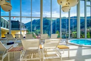 Innenpool im Salzburger Hof mit weißen Liegen und bodentiefen Fenstern mit Blick auf die Berge von Bad Gastein.