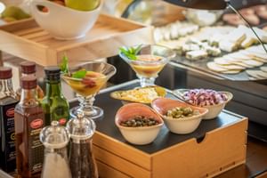 Frühstücksbuffet in der Finca Son Roig mit Schalen voller Oliven, Käse, Zwiebeln, Cocktails, Obst und Käseplatte im Hintergrund.
