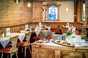 Intérieur de restaurant autrichien traditionnel avec murs en bois, suspensions, tables dressées avec linge blanc et buffet en bois.