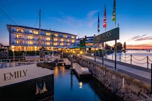 Bad Horn Hotel und Spa beleuchtet in der Dämmerung am Bodenseeufer mit Hafen, Flaggen und Boot namens Emily im Vordergrund.