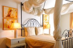 Elegantes Doppelzimmer im Hotel Moliceiro Aveiro mit schmiedeeisernem Himmelbett, weißen Vorhängen, orangen Kunstwerken und Nachttischlampen.