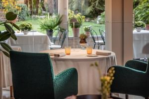 Eleganter Restauranttisch mit grünen Samtstühlen, weißer Tischdecke, orangen Gläsern und Gartenblick im Regina Adelaide Hotel in Garda.
