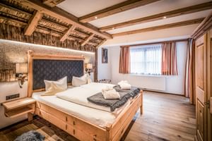 Chambre double rustique avec poutres apparentes, mur en pierre, lit en bois, literie blanche et décor alpin à l'Hôtel Hauserei Steeg.