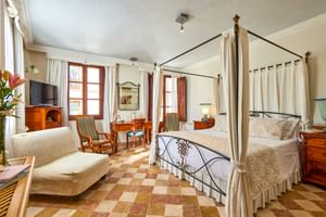 Chambre double spacieuse avec lit à baldaquin en fer, sol carrelé en damier, meubles en bois, canapé beige et fenêtres avec rideaux blancs à Pollença.