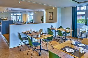 Moderner Frühstücksraum im Hotel Upstalsboom Langeoog mit grünen Stühlen, Holztischen mit Servietten und Gläsern, Buffettheke.