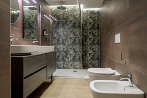 Modernes Badezimmer in der Villa Dirce Limone mit geometrisch gemusterter Duschwand, schwebendem Waschtisch, Spiegel, WC, Bidet und beigen Bodenfliesen.