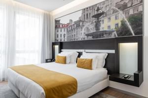 Modernes Doppelzimmer im Hotel Jupiter Lisboa mit weißem Bett, gelben Akzentkissen, schwarzer Kopfteileinheit und Lissabon-Wandbild.