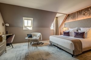 Modernes Mansarden-Doppelzimmer mit Dachschräge, Dachfenster, grau gepolstertem Bett, Sitzecke und Holzbalken-Akzentwand im Hotel Fleur de Loire.