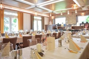 Eleganter Frühstücksraum im Hotel Ertl in Spittal mit weißen Tischen, braunen Stühlen, Weingläsern und moderner Deckenbeleuchtung.