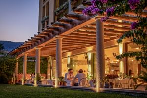 Abendansicht der Regina Adelaide Garda Hotel-Terrasse mit Holzpergola, beleuchteten Säulen, speisenden Gästen und lila Bougainvillea-Blüten.
