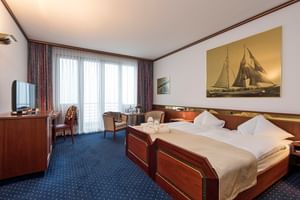 Elegantes Hotelzimmer im Bad Horn mit zwei Betten, nautischen Kunstwerken, Holzmöbeln, blauem Teppich und großen Fenstern mit Vorhängen.