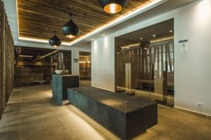 Espace spa luxueux avec bancs en pierre sombre, plafond en bois, cabine de sauna en verre et éclairage suspendu moderne au Schwarzer Adler St. Anton.