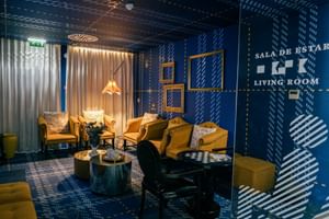 Modernes Wohnzimmer im Macarico Beach Hotel mit blauen gemusterten Wänden, gelben Sesseln, rundem Couchtisch und Pendelleuchten.