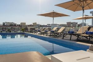 Dachpool im Hotel Jupiter Lisboa mit blau gefliesten Pool, beigen Sonnenliegen, cremefarbenen Sonnenschirmen und Stadtblick.