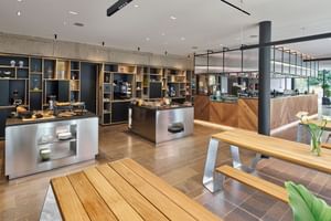 Moderner Frühstücksbuffetbereich mit Holzregalen, Edelstahltheken und Holzesstischen in einem zeitgenössischen Hotelrestaurant.